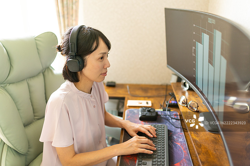 一位戴着耳机的女性在家中使用电脑工作图片素材