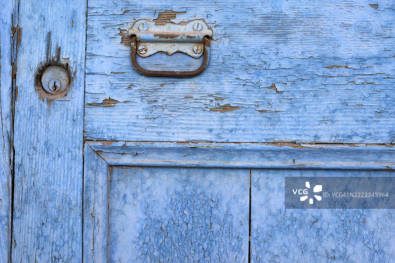 风化的蓝色门细节，显示出剥落的油漆和生锈的把手图片素材