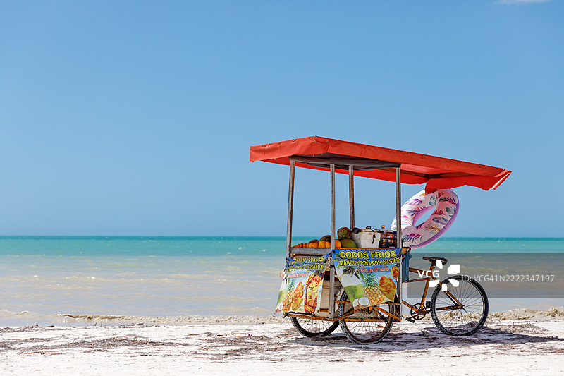 海滩小贩的自行车货车，出售新鲜水果如芒果和椰子，背景是碧蓝的海水。图片素材