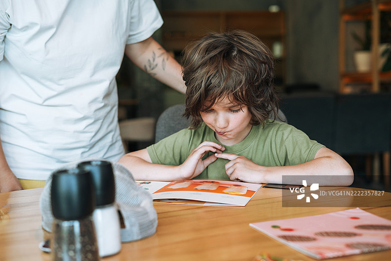 一个6到7岁的小男孩和他的母亲在咖啡馆选择菜单上的食物图片素材