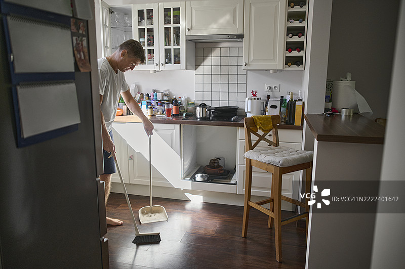 男人在家里的厨房里扫地图片素材