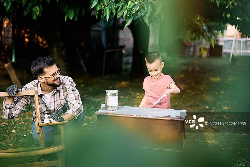 快乐的男孩和他的父亲在后院进行家具修复。图片素材