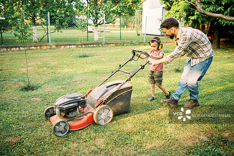 可爱的小男孩正在学习如何用割草机割草。图片素材
