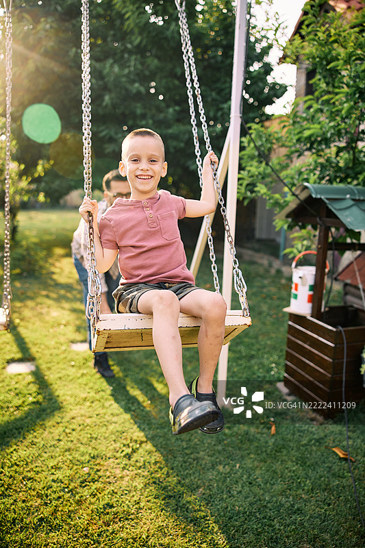可爱的男孩在后院与父亲一起玩秋千。图片素材