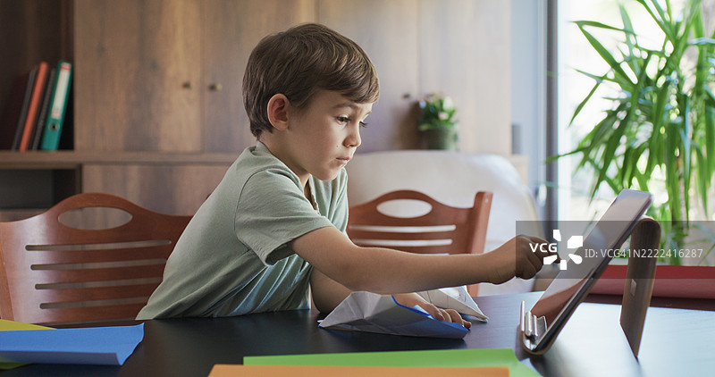 男孩正在使用彩色纸折叠玩具，按照数字平板上的视频教程步骤进行。图片素材