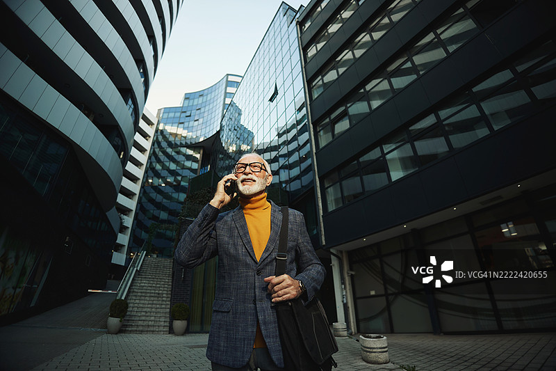 一位英俊的高级商务男士在城市中走动，正在打电话。图片素材
