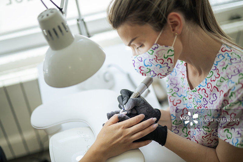 专业美甲师使用电动指甲锉为客户修整指甲。图片素材