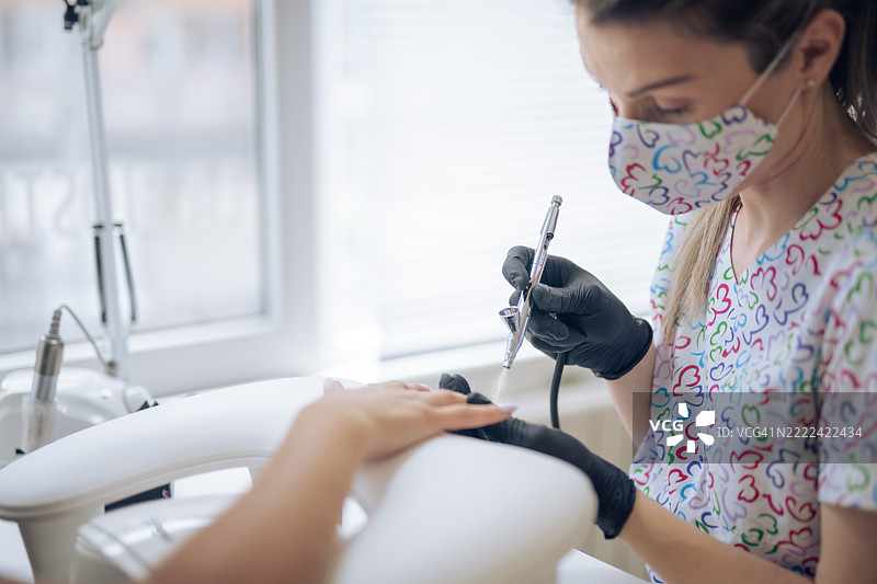 美甲师使用喷枪为客户的指甲涂抹指甲油。图片素材