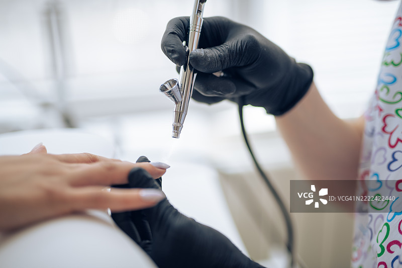 美甲师使用喷枪为客户的指甲涂抹指甲油。图片素材