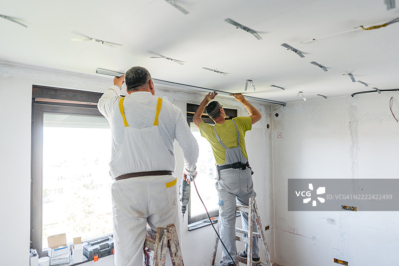 两名成熟工人在空置的正在装修的公寓内安装石膏板天花板。图片素材
