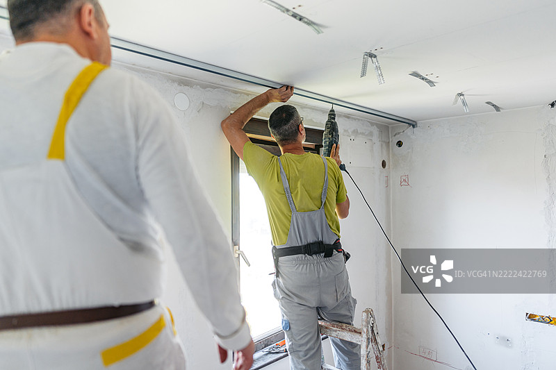 两名成熟工人在空置的正在装修的公寓里用电钻在天花板上安装石膏板型材图片素材