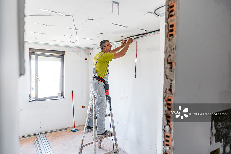 成熟工人在空置的正在装修的公寓里安装石膏板天花板。图片素材