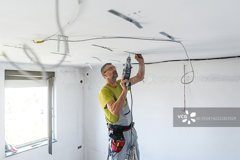 成熟工人在空置的正在翻新的公寓天花板上用电钻安装干墙间隔器图片素材