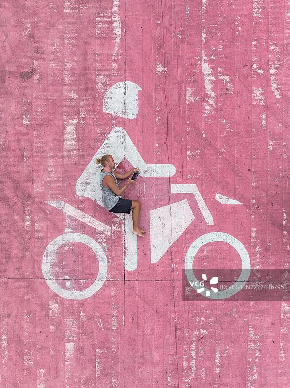一名男子躺在涂有粉色摩托车标志的公路上，假装骑车，巴厘岛，印度尼西亚图片素材