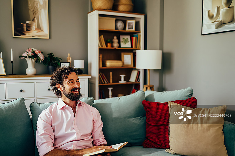 微笑的男人在客厅的沙发上放松地阅读一本书图片素材