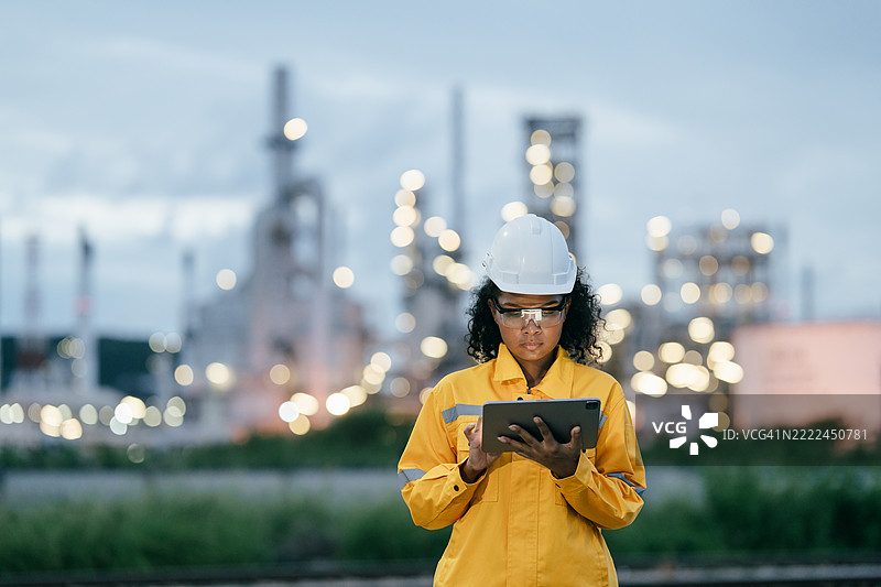 黄昏时分，穿着防护服的女性工程师在工业厂房内使用平板电脑图片素材