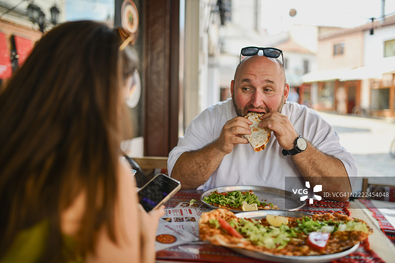 饥饿的男性享用传统土耳其菜，而女性则无视他，专注于手机发信息。图片素材