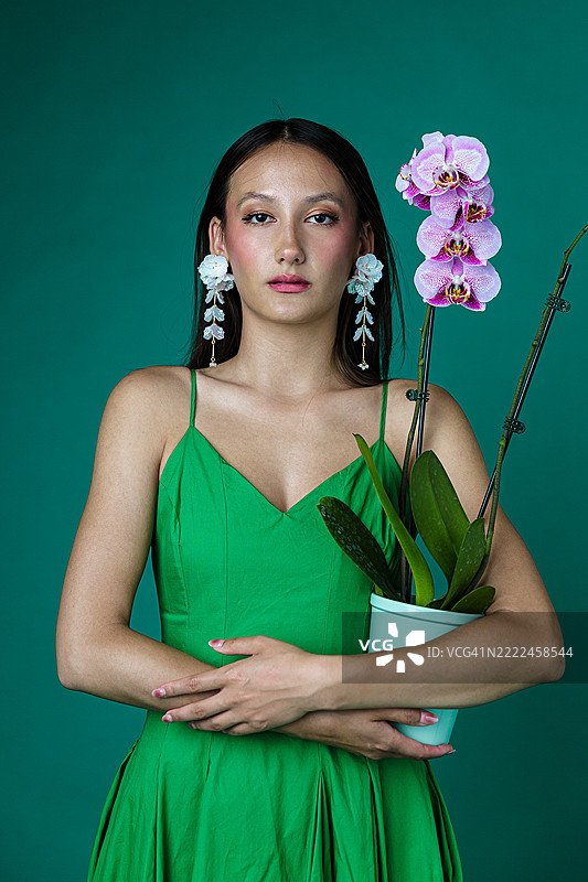 穿着绿色连衣裙的时尚女性手持兰花植物图片素材