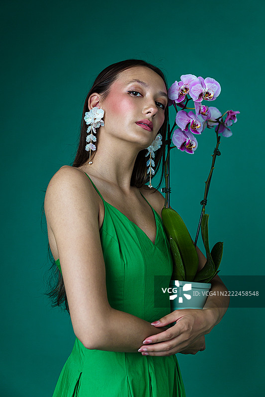 穿着绿色连衣裙的时尚女性手持兰花植物图片素材