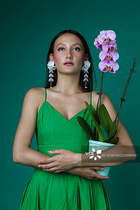 穿着绿色连衣裙的时尚女性手持兰花植物图片素材