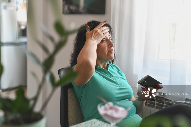 一位女性在激烈的游戏回合后，一边玩手机游戏一边擦汗图片素材