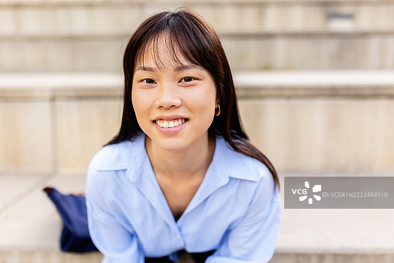年轻的亚洲女性微笑着，向前倾身坐在台阶上图片素材