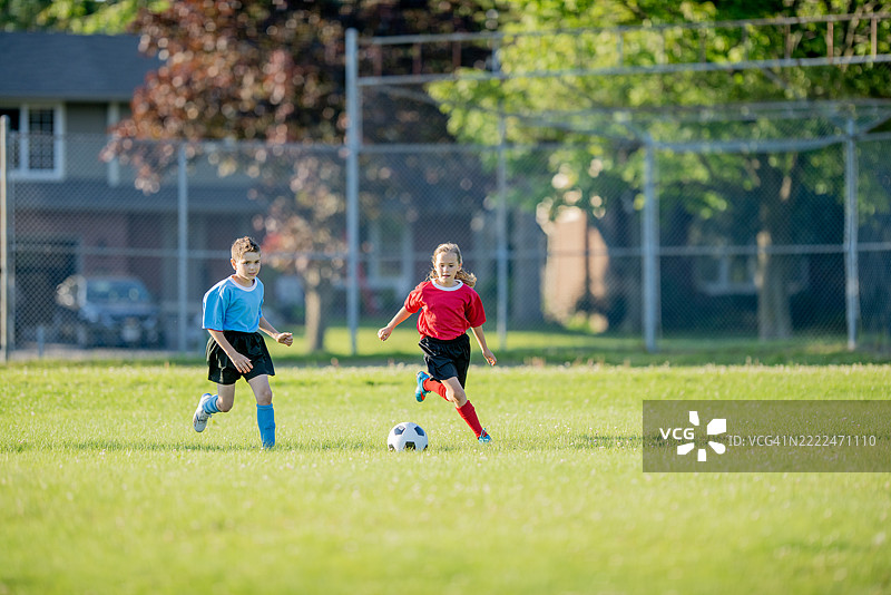 两个孩子在阳光明媚的户外球场上踢足球图片素材