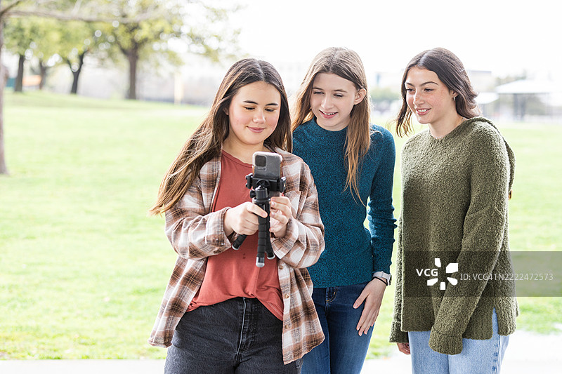 三名青少年女孩在户外使用智能手机三脚架图片素材