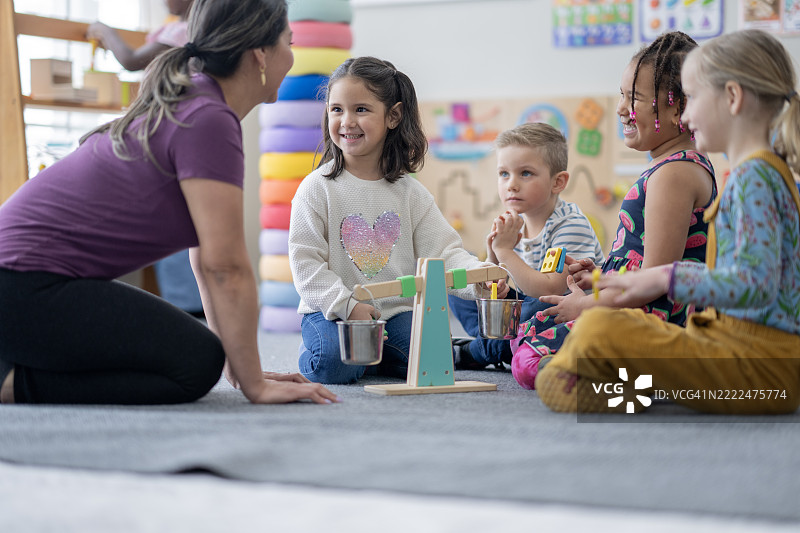 教师与孩子们在课堂学习活动中互动，使用玩具秤。图片素材