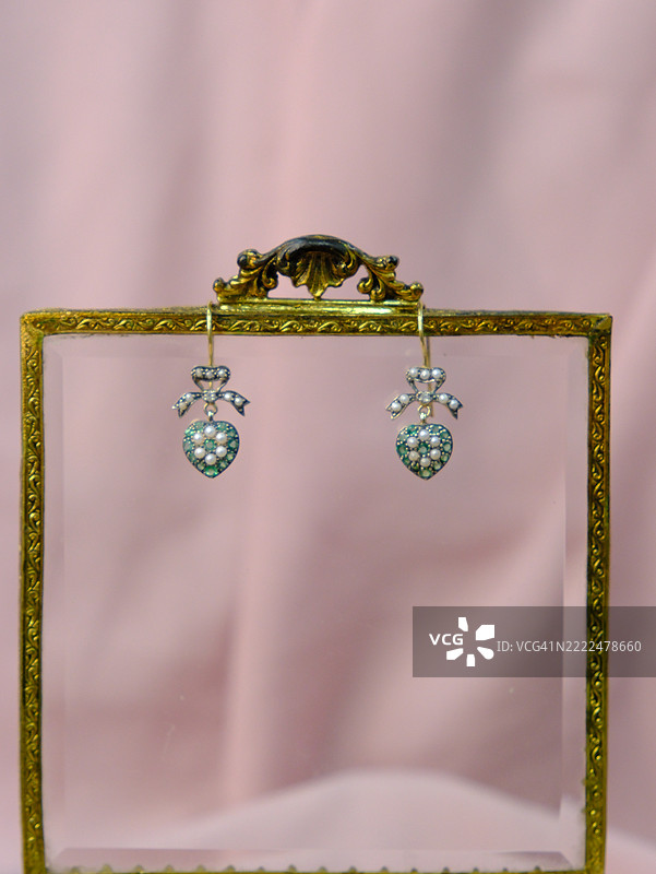 优雅的心形复古耳环，配有珍珠和绿色宝石，悬挂在华丽的玻璃盒上，浪漫的珠宝展示，适用于产品摄影和编辑使用图片素材