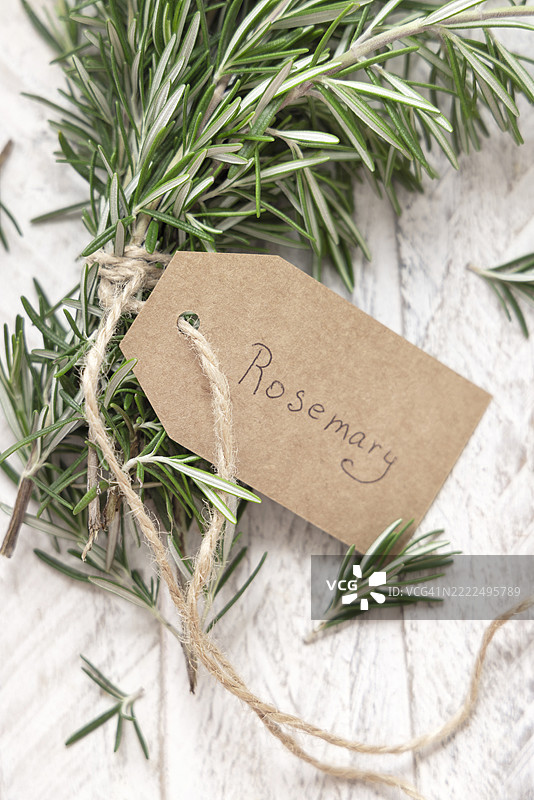 新鲜的绿色迷迭香枝条，带有牛皮纸标签，放在白色风化木桌上，俯视图，布林迪西，普利亚，意大利图片素材