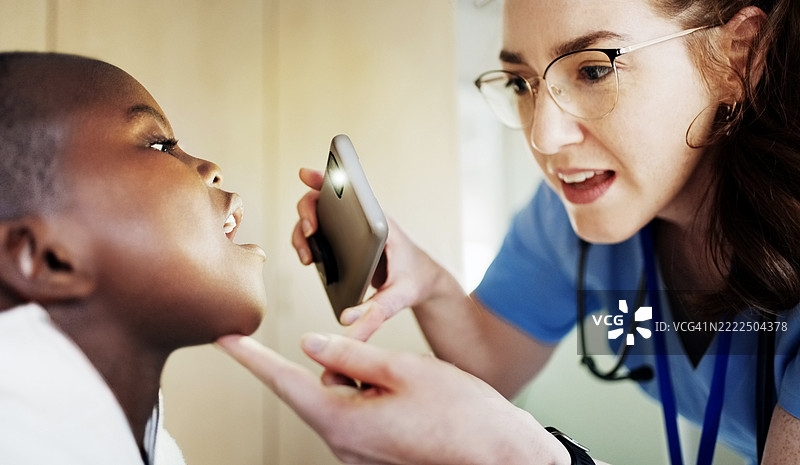 儿科医生在诊所里用手机手电筒检查小男孩的喉咙图片素材