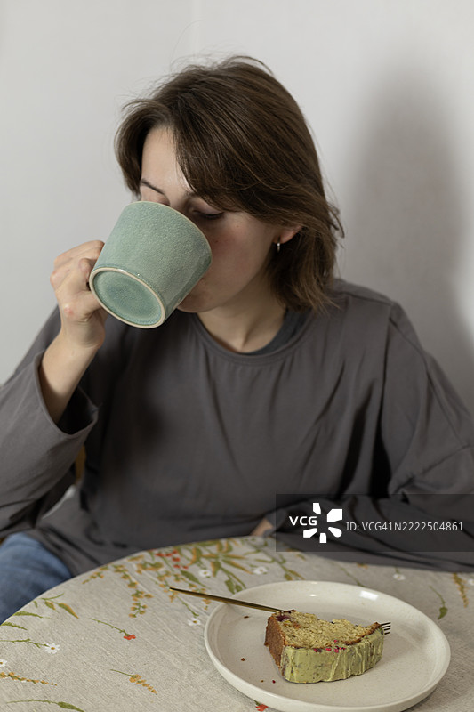 一位年轻女士在简约的室内环境中，享受甜点和温暖饮品，表情平静，周围环境舒适。图片素材