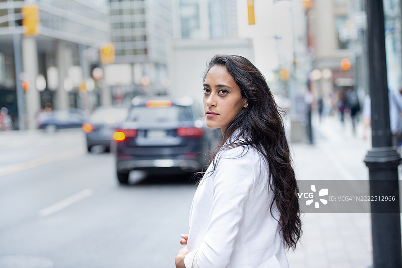 自信的女性穿着白色夹克，白天在城市街道上站立图片素材