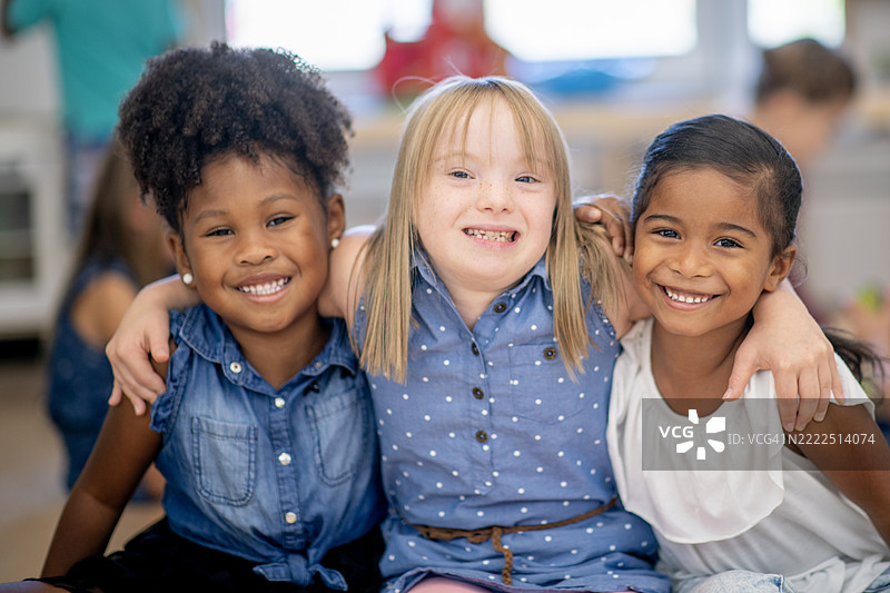 三个不同种族的孩子在愉快的教室环境中微笑并拥抱图片素材