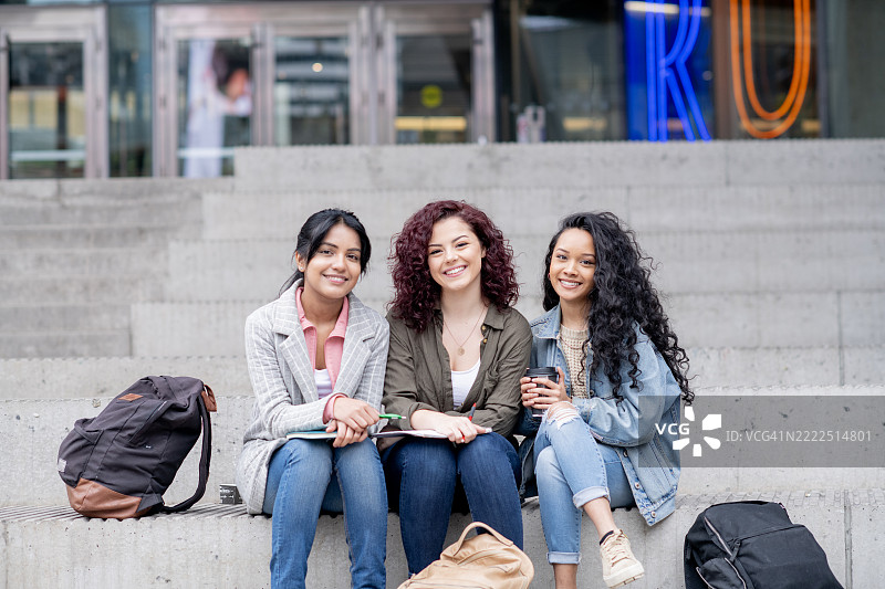 三位朋友在大学台阶上放松，开心地微笑在一起图片素材