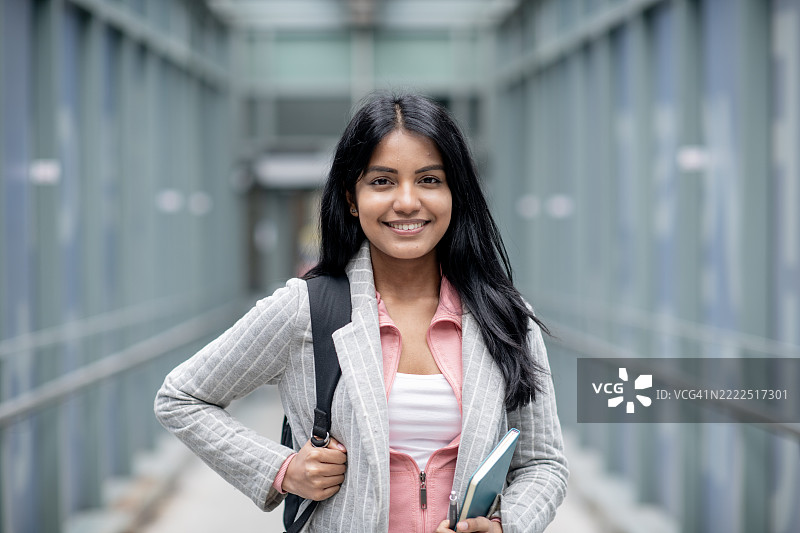 自信的学生在校园走廊里微笑着手握书本图片素材
