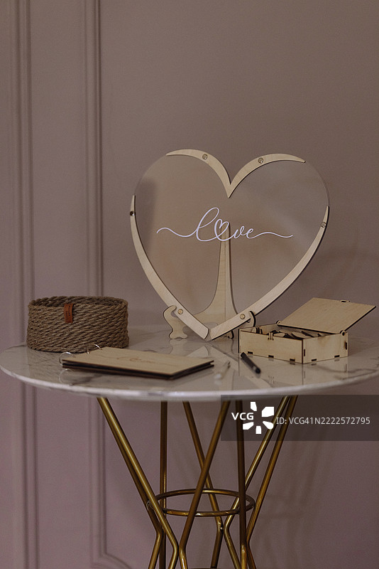 婚礼嘉宾留言簿桌，圆形大理石台面上放着透明心形标志，背景是粉色墙壁图片素材