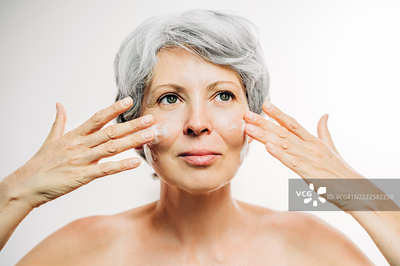 成熟的女性在化妆间给脸部涂抹面霜。图片素材