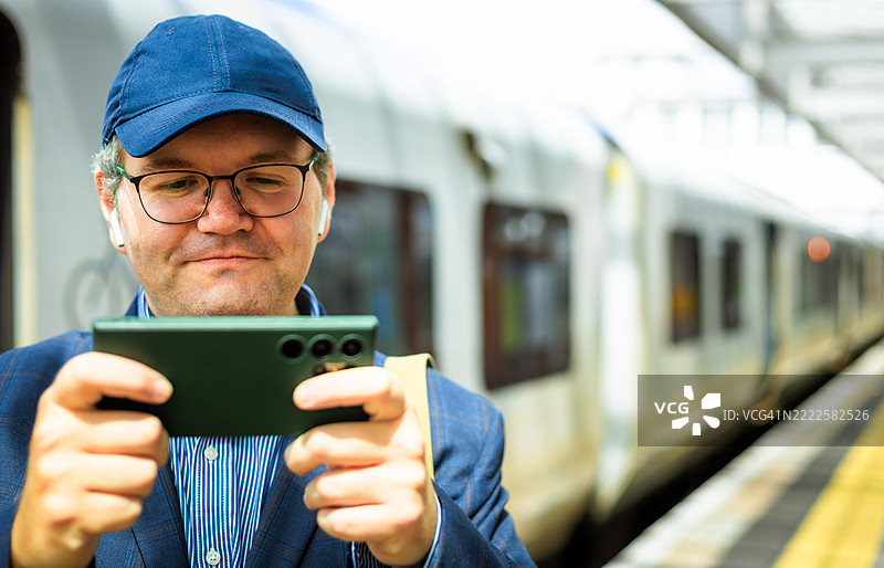 中年男子在火车站台候车时玩手机游戏图片素材