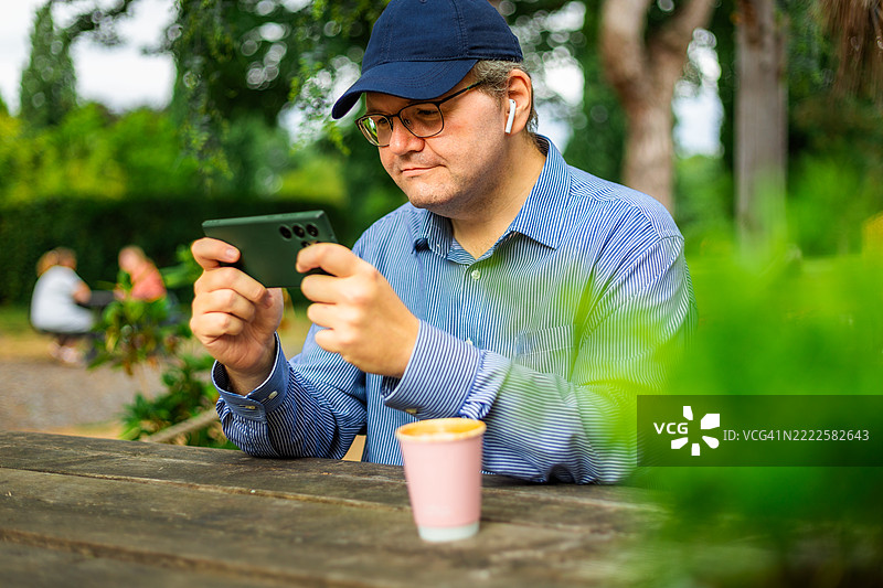 中年职业男性在咖啡馆户外桌旁玩手机游戏图片素材