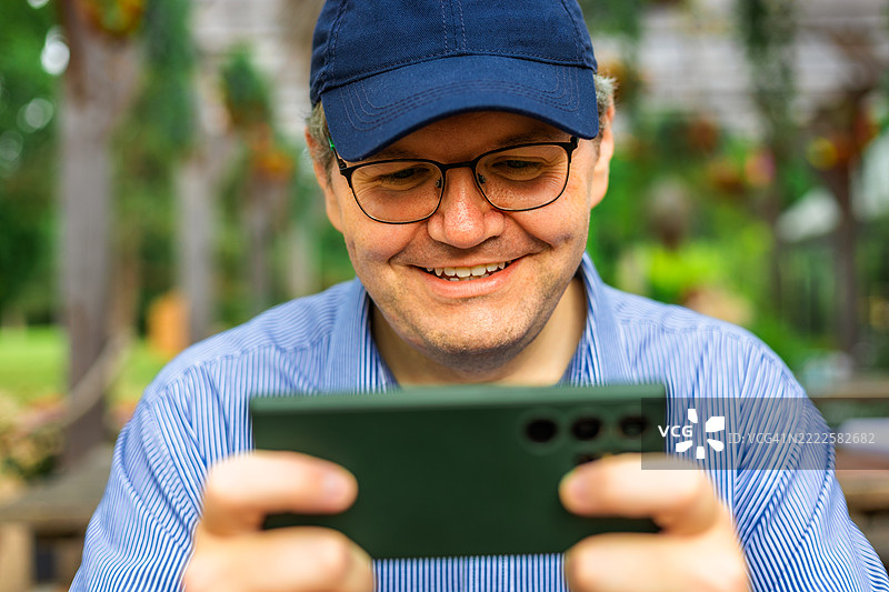 中年职业男性在咖啡馆的户外餐桌旁玩手机游戏图片素材