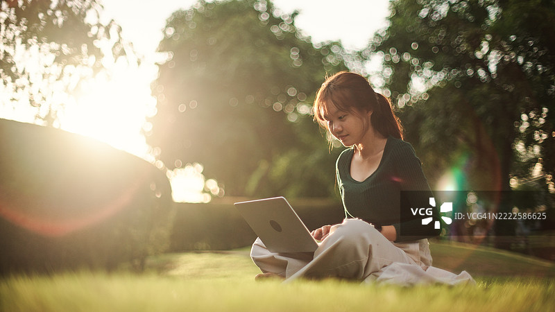 青少年在公园使用笔记本电脑。图片素材