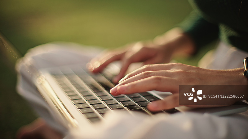 在日落时分户外用手在笔记本电脑上打字。图片素材