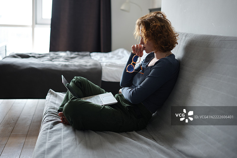 自由职业者的疲惫。疲惫的女性坐在沙发上，使用笔记本电脑在家远程工作。过度劳累的症状。在家工作与心理健康。图片素材