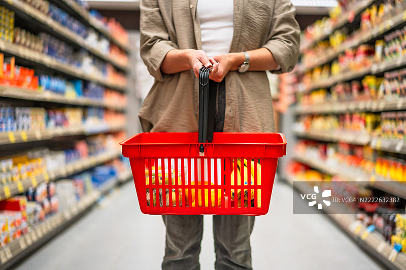 女性在超市的食品走廊中提着购物篮图片素材