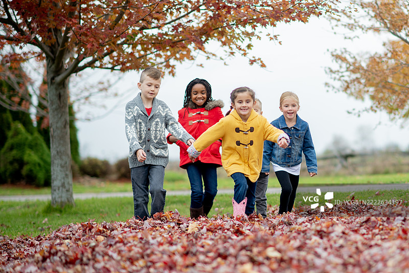 一群快乐的孩子在清爽的秋天里玩落叶图片素材