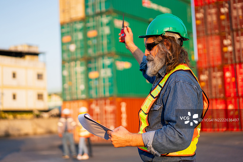 工头在港口检查集装箱，以监督货物运输和物流。涉及航运、进口和出口行业。图片素材