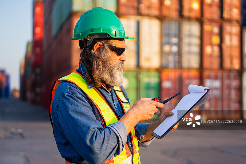 工头在港口检查集装箱，以监督货物运输和物流。涉及航运、进口和出口行业。图片素材