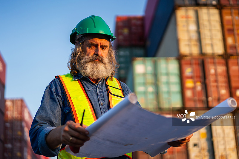 工头在港口检查集装箱，以监督货物运输和物流。涉及航运、进口和出口行业。图片素材